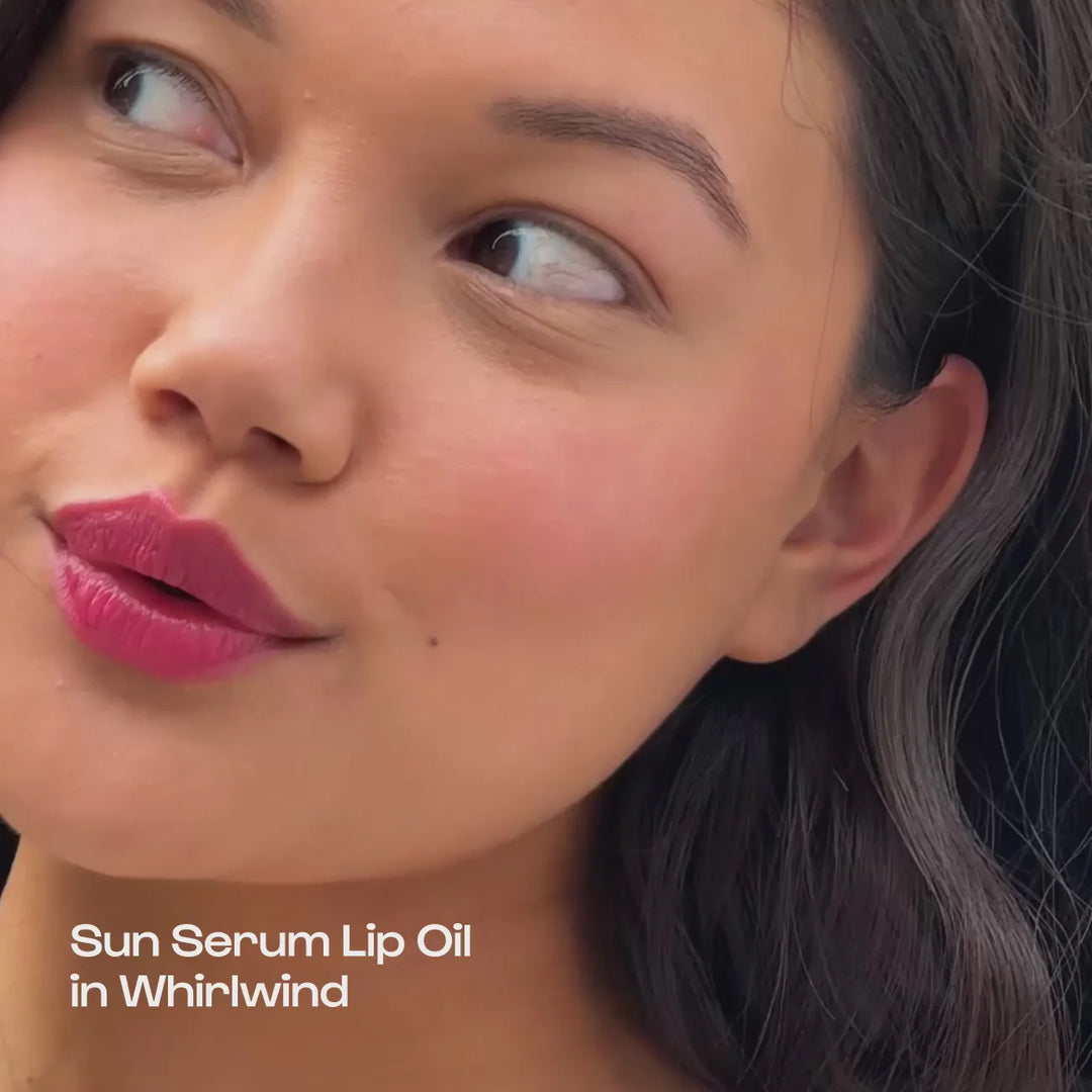 Digital commercial photograph for Sun Serum Lip Oil featuring a woman’s close-up portrait with vibrant magenta lips in Whirlwind, dewy glowing cheeks, and long dark wavy hair