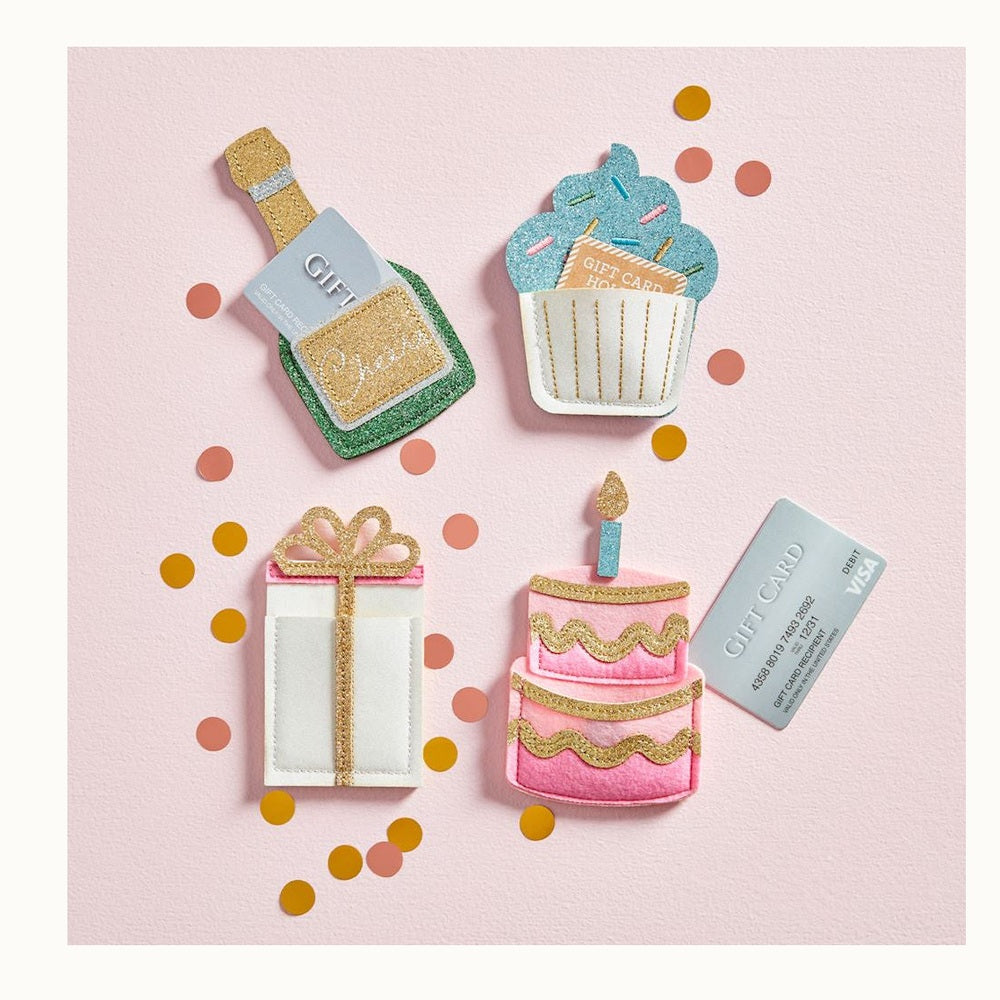 Handcrafted felt and glitter gift card holders featuring a champagne bottle, blue cupcake, and pink tiered cake are arranged on a pink textured background with sparkly gold accents and scattered metallic confetti