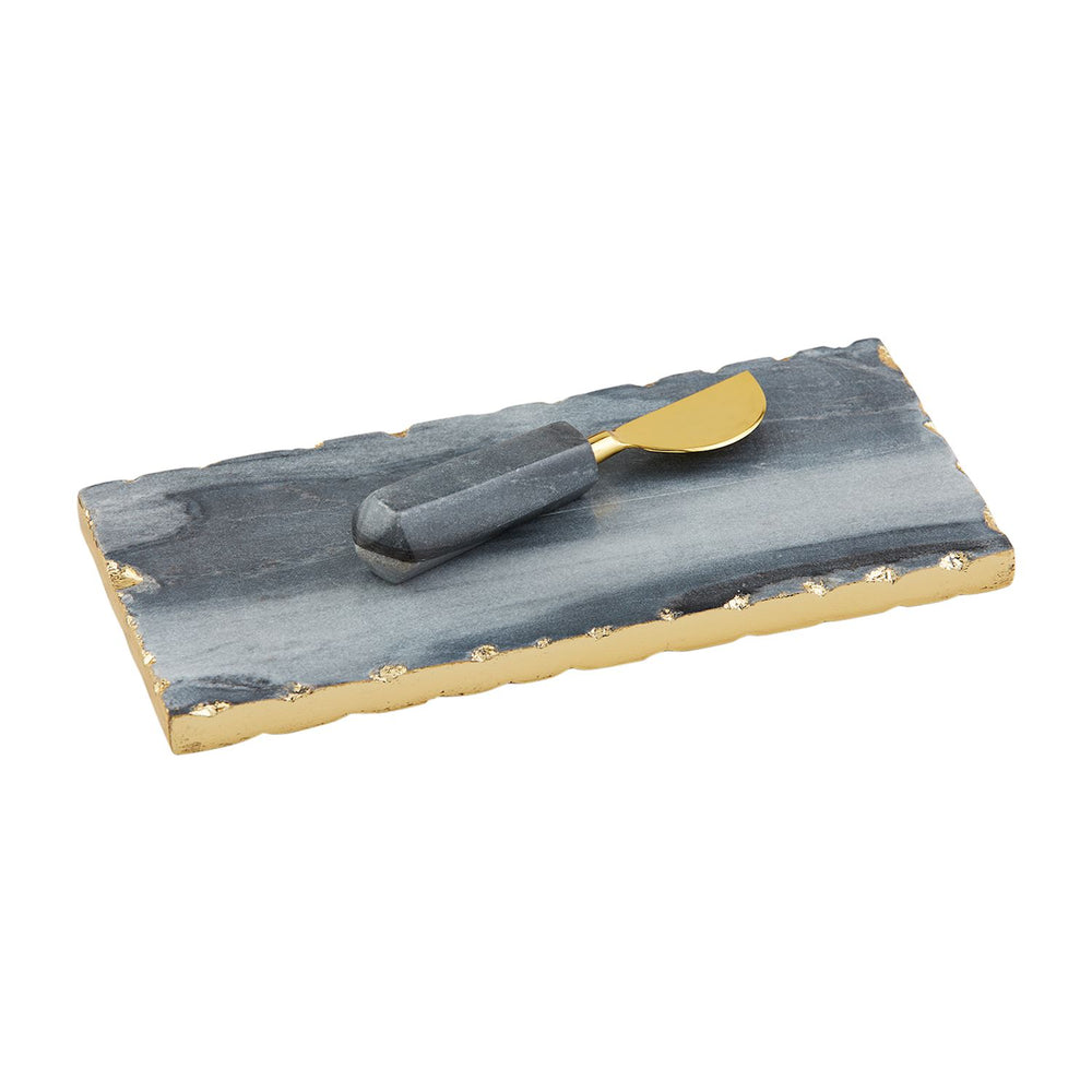 Marble and gilded metal cheese board and spreader set on a white background featuring raw gold-foiled scalloped edges, blue-grey stone veining, and a spreader with a matching hexagonal marble handle