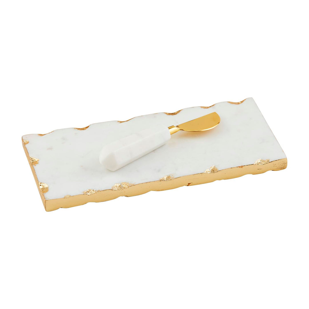 Marble and gold-leaf artisanal serving set featuring a white rectangular cheese board with raw gilded edges and a matching spreader with a faceted marble handle on a white studio background