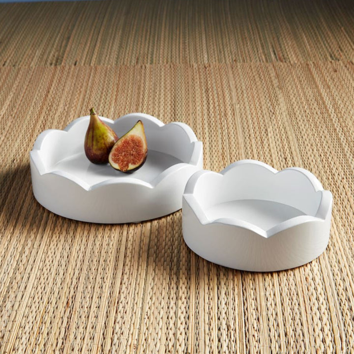 Handcrafted white scalloped trays featuring a whole and sliced fig with a vibrant red interior resting on a textured natural woven straw mat