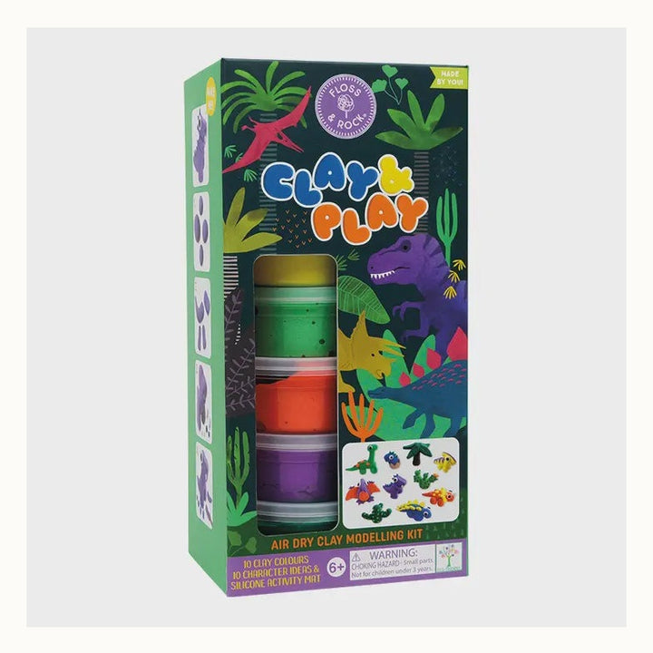 Packaging design by Floss &amp; Rock for a dinosaur-themed air dry clay modelling kit set in a prehistoric jungle, featuring a purple Tyrannosaurus Rex, a pink Pterodactyl, and five stacked tubs of vibrant yellow, green, and orange clay alongside a display of small clay dinosaur models