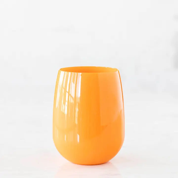 Photograph of a vibrant orange stemless tumbler centered on a white reflective surface featuring a high-gloss finish and distinct vertical window light reflections along its curved silhouette