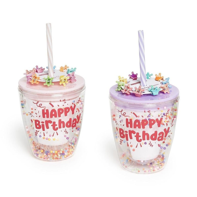 Product photograph of two plastic double-walled tumblers with pink and purple lids featuring Happy Birthday text in red bubble letters alongside colorful crown-shaped hair clips and confetti-filled bases against a white background