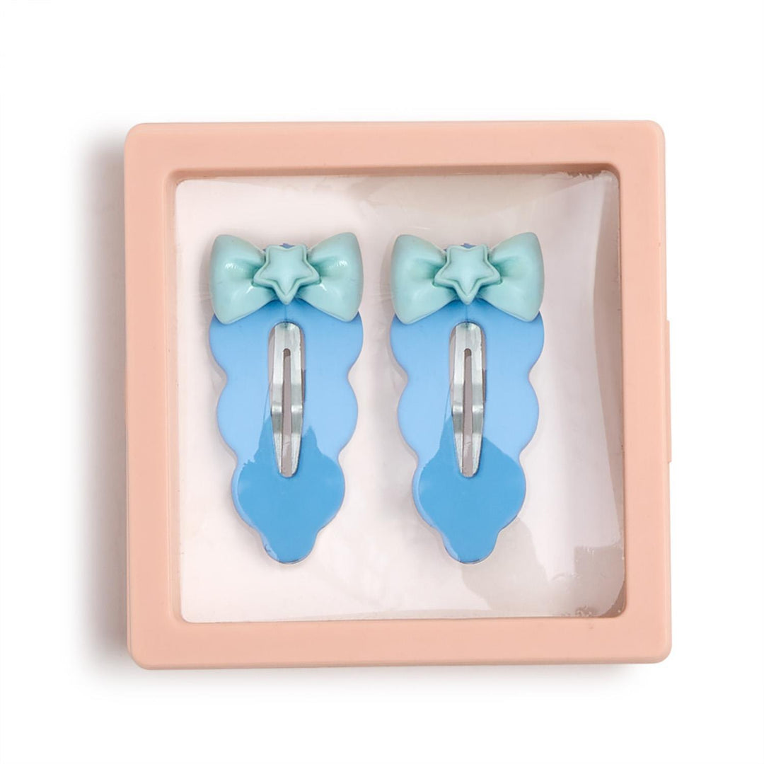 Studio photograph of plastic hair clips featuring blue scalloped edges and mint green bows with star centers displayed inside a square pink floating frame