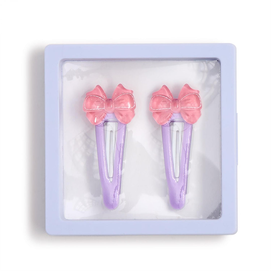 Product photograph of two resin hair accessories centered in a square lavender display box featuring snap-style clips and translucent pink bows with white decorative stitching