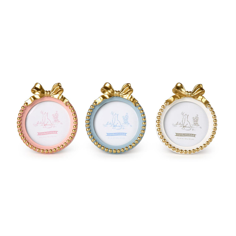 Resin decorative frames by Cupcakes & Cartwheels featuring three small round photo frames in pastel pink, light blue, and cream white accented with ornate gold ribbon bows and beaded borders set against a plain white background