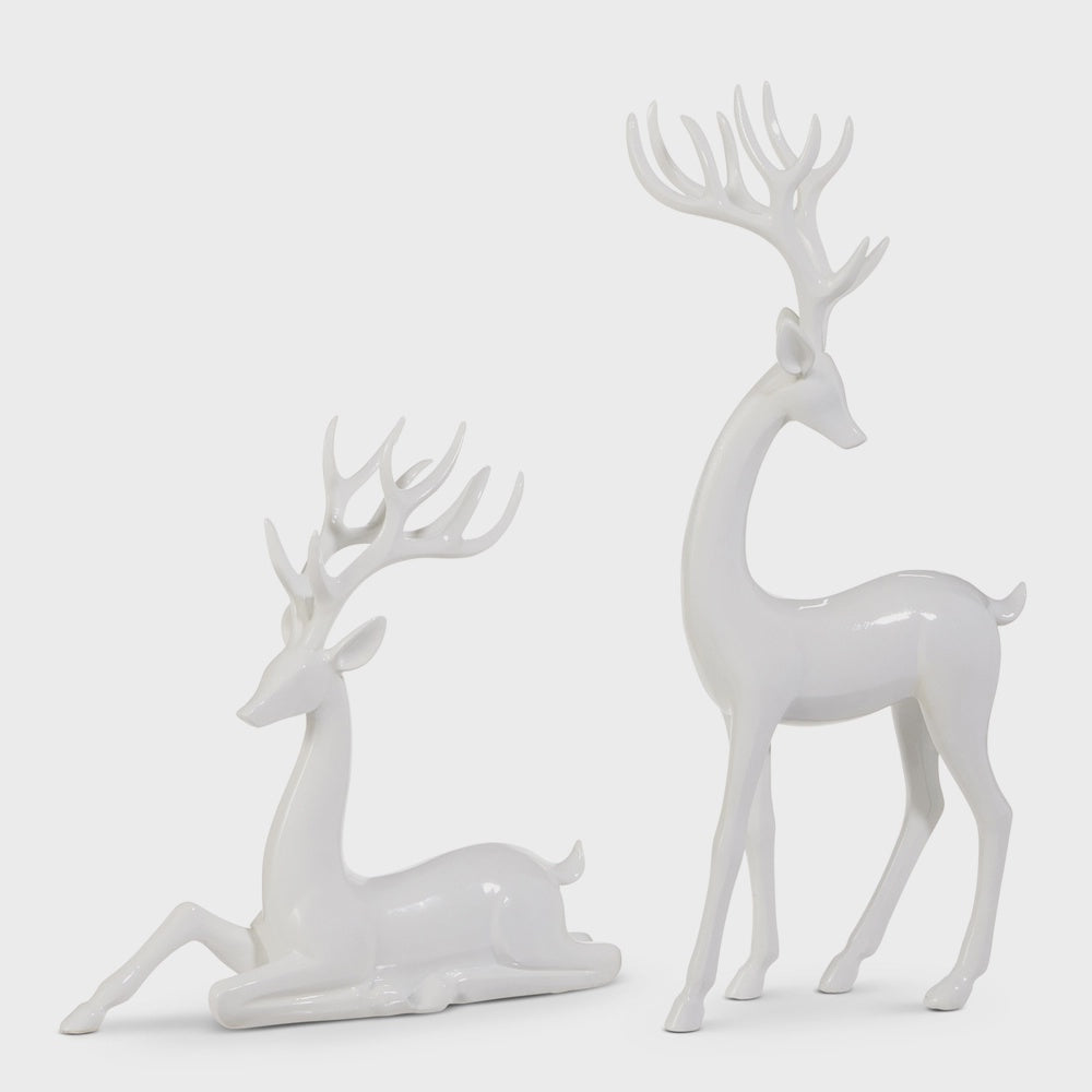 Ceramic sculptures of a standing and reclining white deer in a studio setting featuring a glossy finish, elegant elongated necks, and intricate multi-pointed antlers