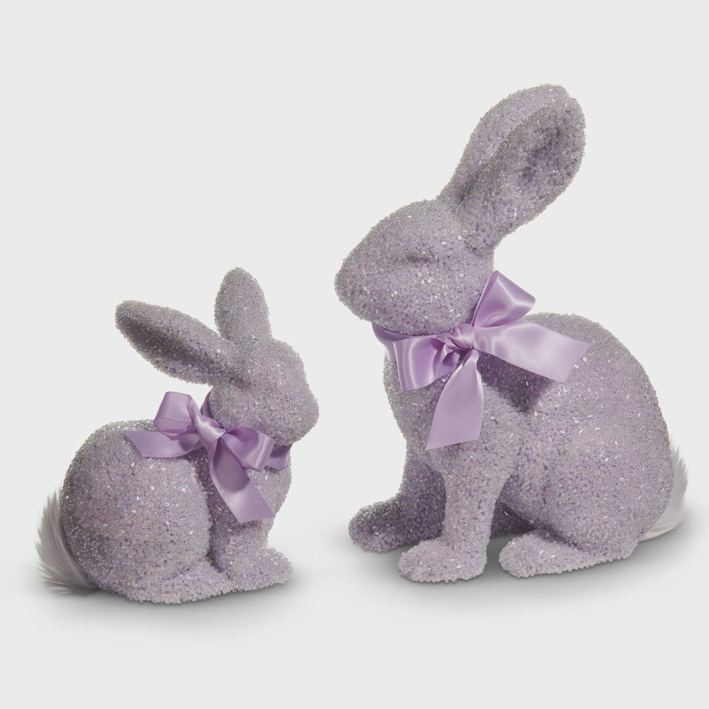 Decorative beaded figurines of two lavender rabbits on a neutral background featuring shimmering crystal-like textures, matching purple satin ribbons, and soft white feather tails