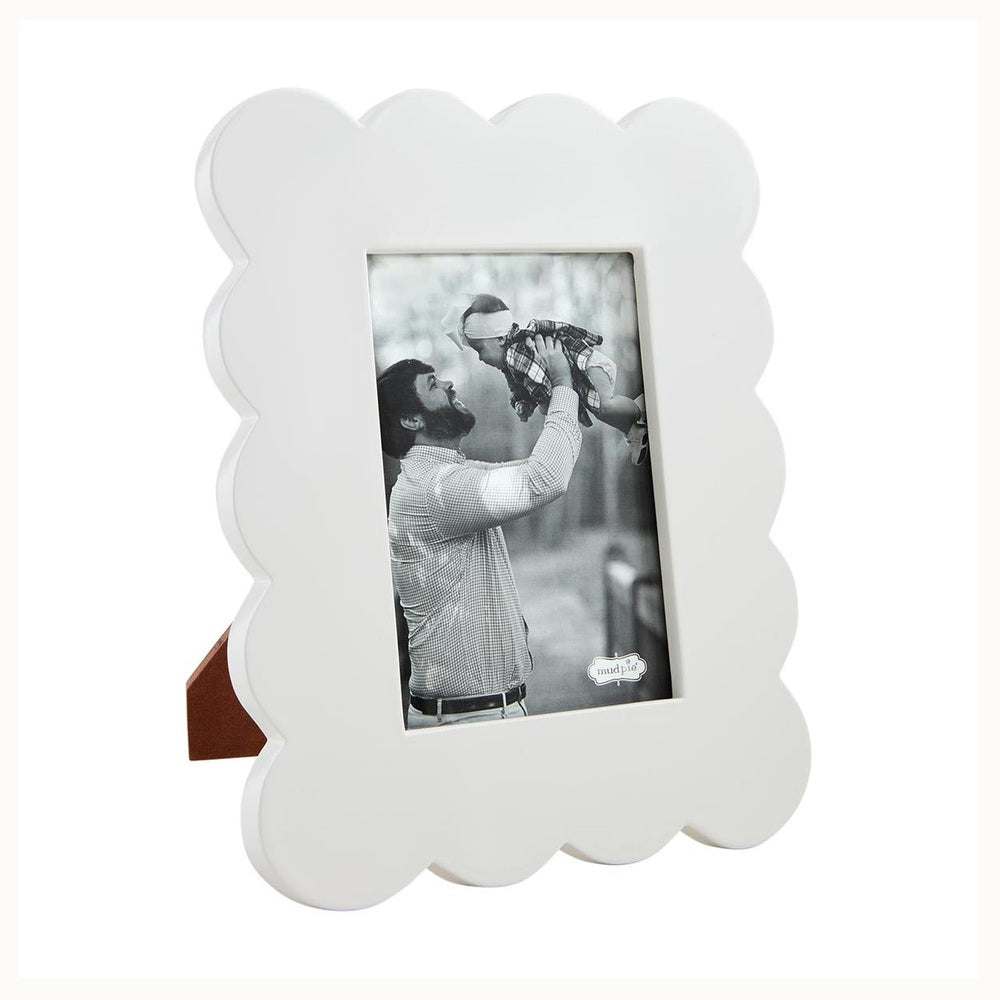 Mud Pie white wood scalloped picture frame showcasing a black and white photo of a bearded father lifting a baby in a wooded area, featuring decorative wavy edges and a brown easel back