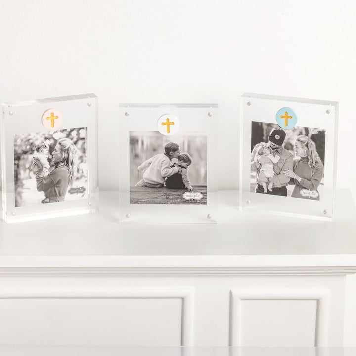 Acrylic magnetic photo frames by Mud Pie displaying three black and white family portraits on a white mantel with pink, white, and blue circular charms featuring gold metallic crosses