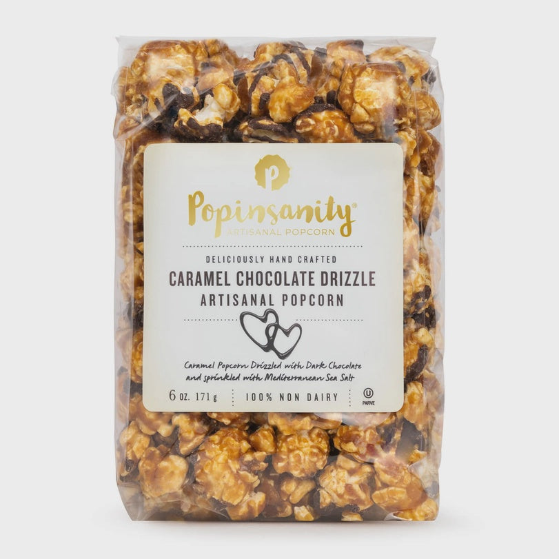 Product photograph by Popinsanity of Caramel Chocolate Drizzle Artisanal Popcorn in a clear bag featuring golden-brown caramel kernels with thin dark chocolate stripes and a cream-colored label with gold-lettered branding and heart icons