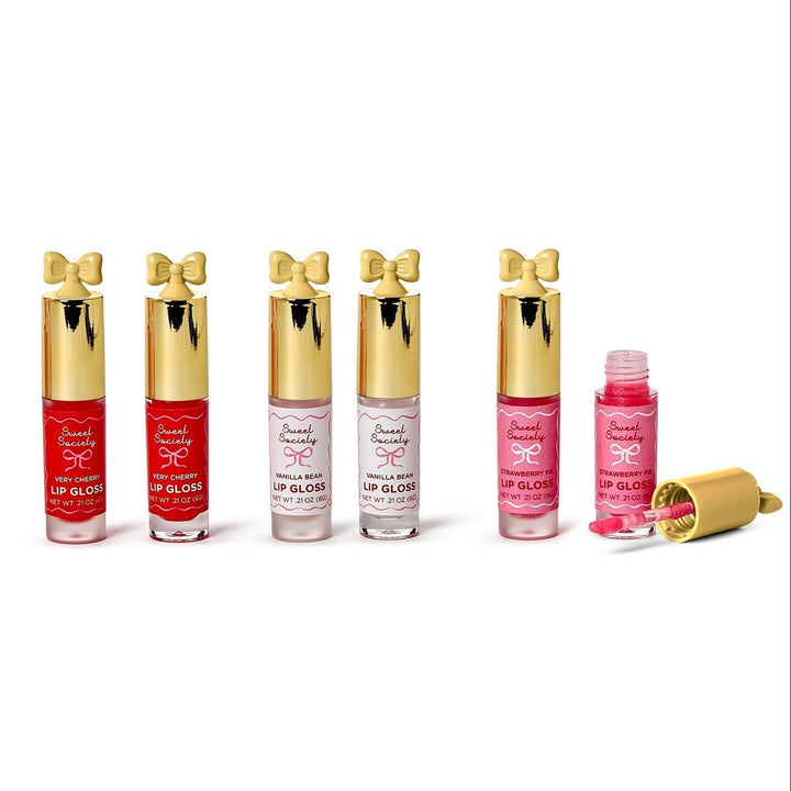 Studio product photography for Sweet Society showcasing six lip gloss tubes on a white background featuring gold bow caps with black drip designs and an open pink Strawberry Pie tube with its applicator wand visible