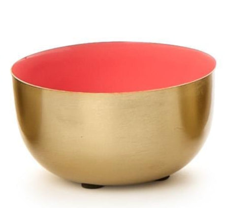 Brushed gold metal bowl featuring a vibrant coral-pink enameled interior and small black rubber feet resting on a plain white studio background
