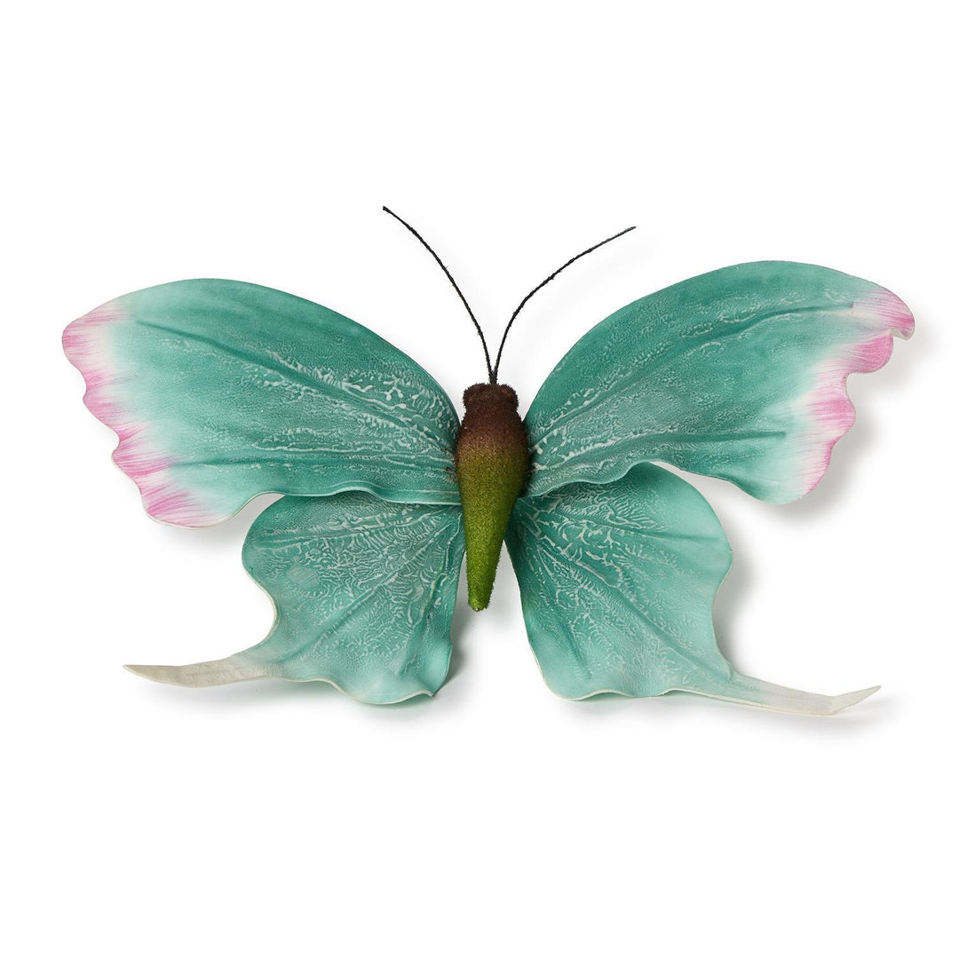 Decorative metal butterfly wall art featuring textured teal wings with soft pink edges and a fuzzy olive green body centered on a white background
