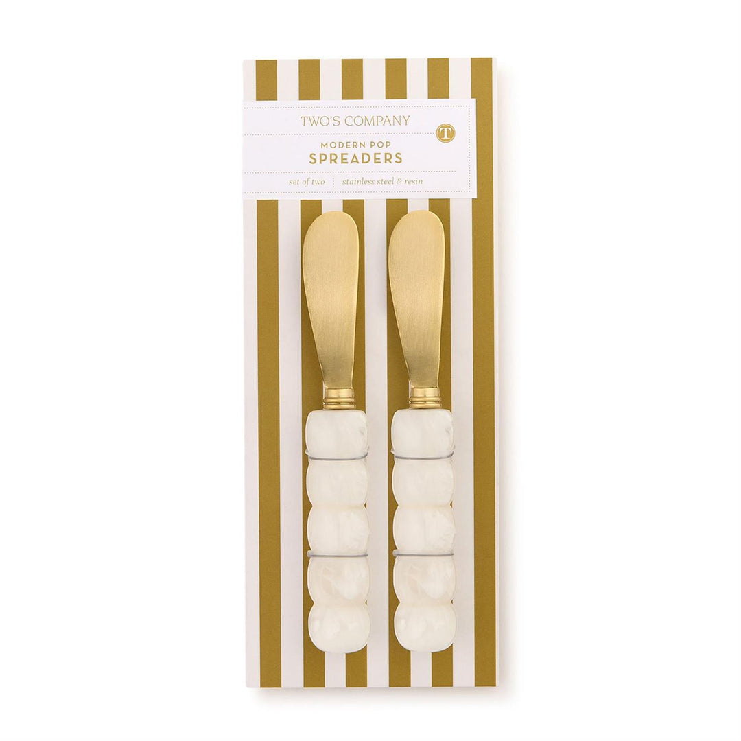 Two’s Company stainless steel and resin Modern Pop Spreaders featuring brushed gold-toned blades and white marbled bobble handles displayed on gold and white striped packaging with a circular T logo