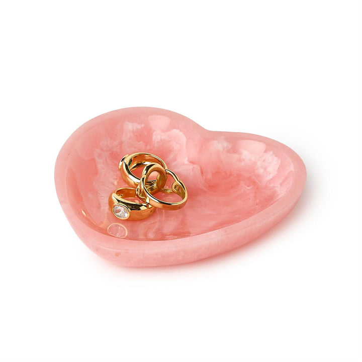 Handcrafted marbled resin heart-shaped trinket dish on a white background featuring swirling bubblegum pink patterns and three gold rings including a band set with a clear faceted gemstone