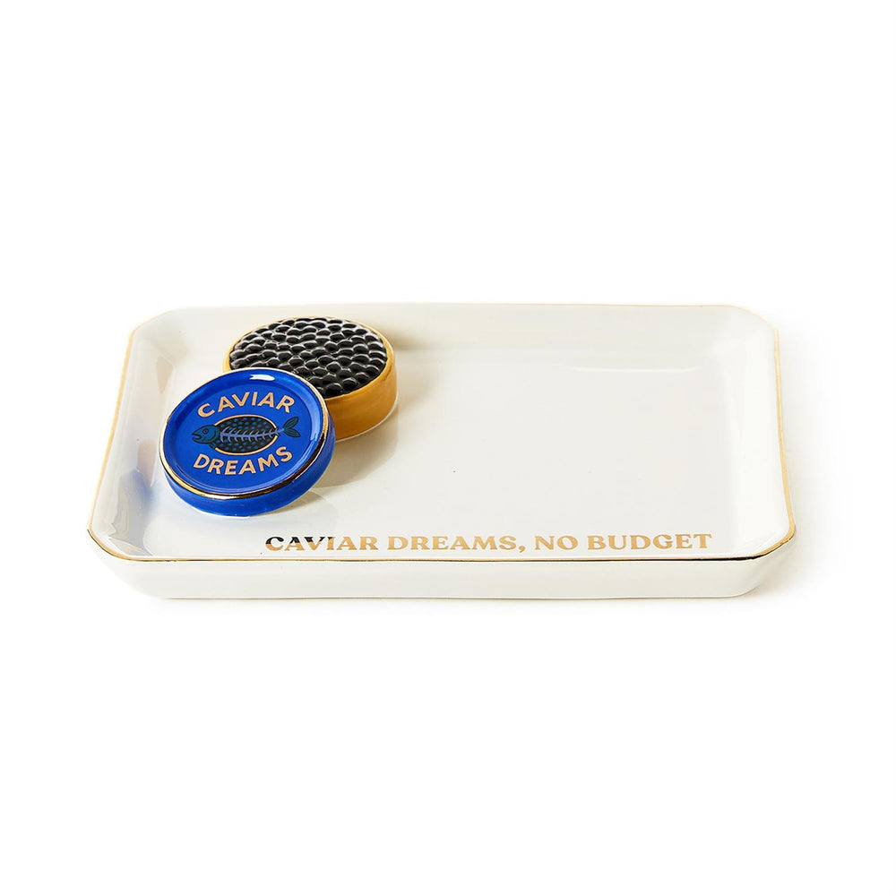 Porcelain tray by Jonathan Adler featuring a white rectangular valet tray with a 3D textured black caviar tin, a vibrant blue lid with a fish bone icon, and gold-toned lettering that reads CAVIAR DREAMS NO BUDGET
