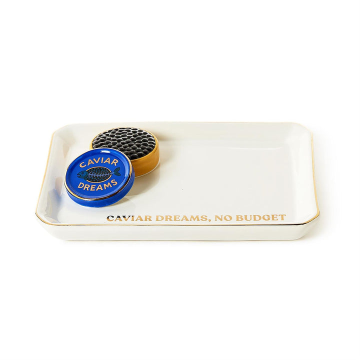 Porcelain tray by Jonathan Adler featuring a white rectangular valet tray with a 3D textured black caviar tin, a vibrant blue lid with a fish bone icon, and gold-toned lettering that reads CAVIAR DREAMS NO BUDGET
