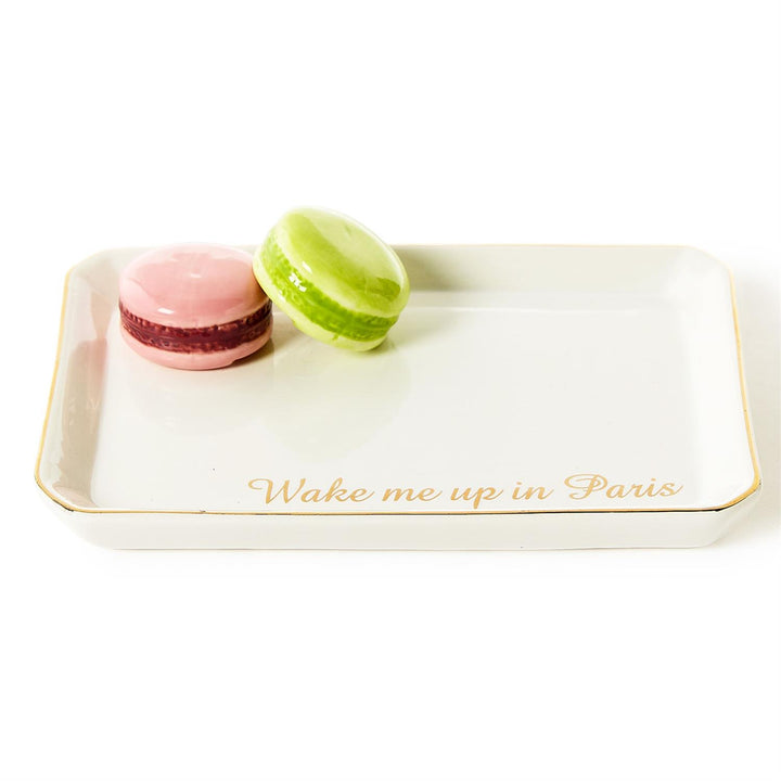 Ceramic trinket tray displaying a pink and lime green macaron with the gold cursive text Wake me up in Paris on a white rectangular surface finished with a gold-leaf rim