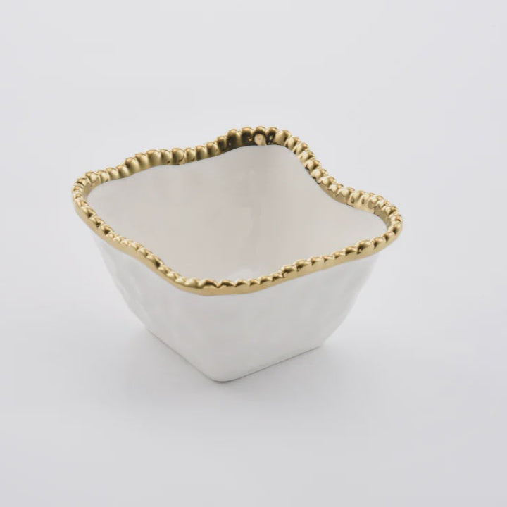 Ceramic bowl by Pampa Bay showcases a small square dish with an organic wavy rim finished in a metallic gold beaded texture set against a minimalist white background
