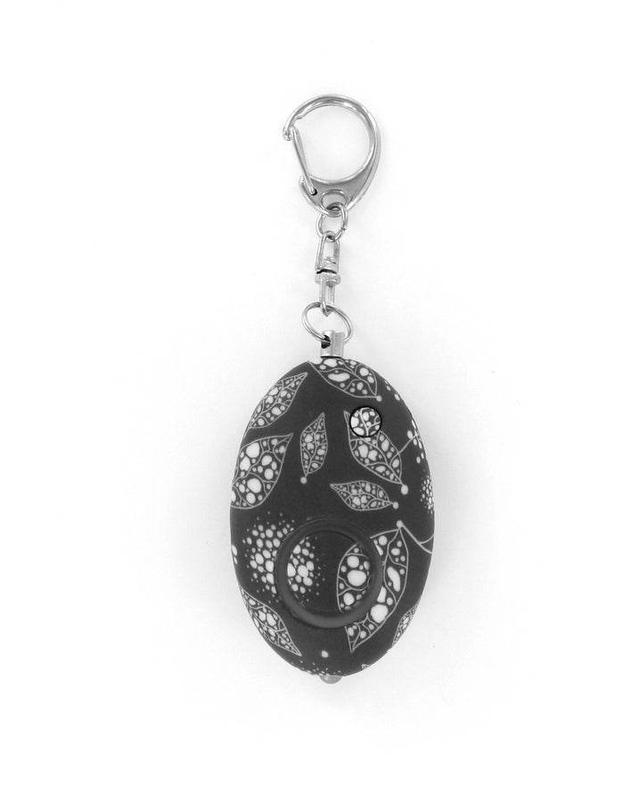 Plastic and metal personal safety alarm featuring an intricate white leaf and bubble pattern on a black egg-shaped body with a silver lobster claw clasp and a small circular LED light on a white background