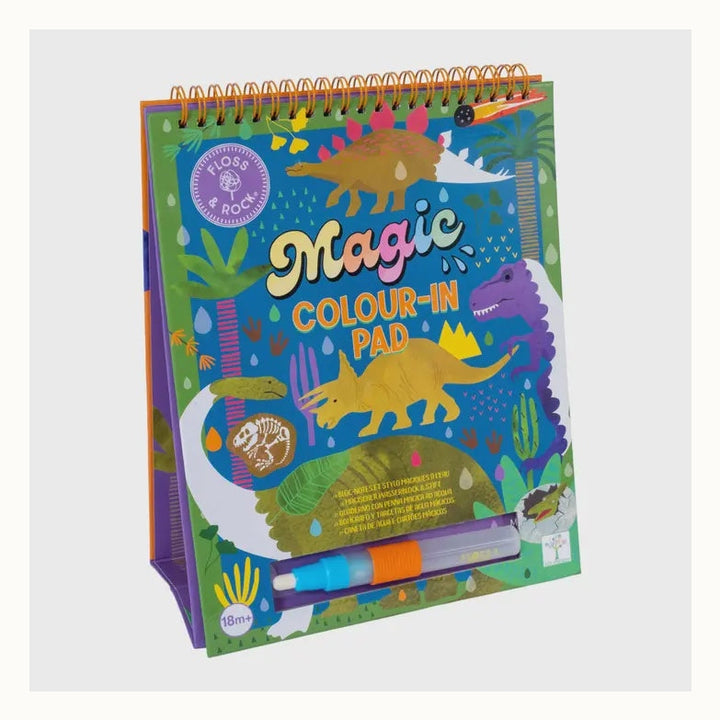 Spiral-bound activity book by Floss &amp; Rock featuring a dinosaur-themed Magic Colour-In Pad set against a volcanic landscape with a vibrant purple Tyrannosaurus Rex, a yellow Triceratops, and a refillable water pen stored in the base