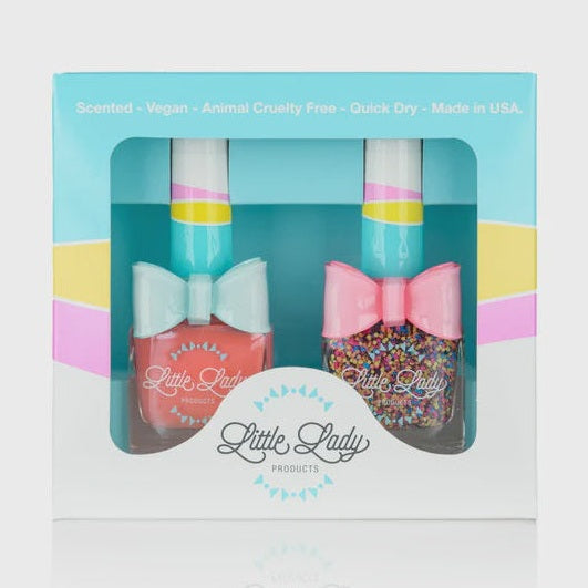 Product photograph by Little Lady Products of a nail polish duo set in a light blue box featuring a solid coral pink bottle with a light blue bow and a multicolored confetti glitter bottle with a pink bow, both showcasing striped caps