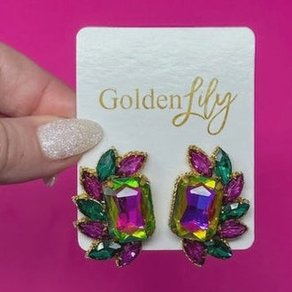 Costume jewelry by Golden Lily featuring a pair of statement earrings with iridescent rectangular center stones and emerald green and fuchsia marquise crystals held on a branded display card against a bright pink background