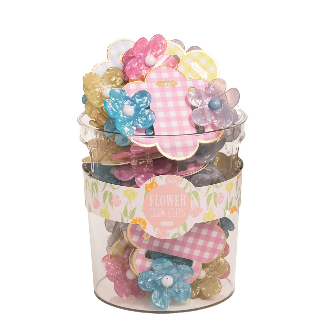Product photograph by Mud Pie of a clear plastic display bucket filled with flower-shaped claw clips in iridescent blue and pink shades featuring white bead centers and pink gingham display tags with a decorative floral label