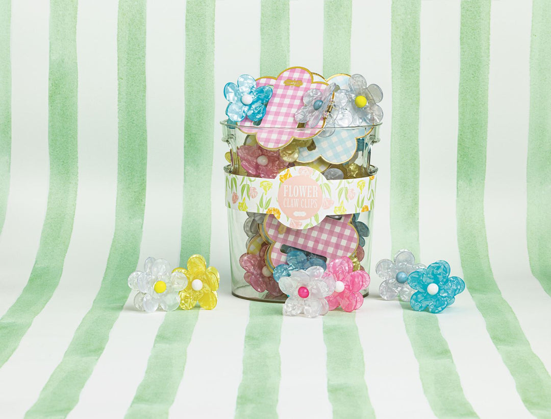 Digital photograph for Mud Pie of marbled flower hair claw clips in a glass jar with a floral label on a green watercolor striped background featuring vibrant yellow centers and pink gingham packaging