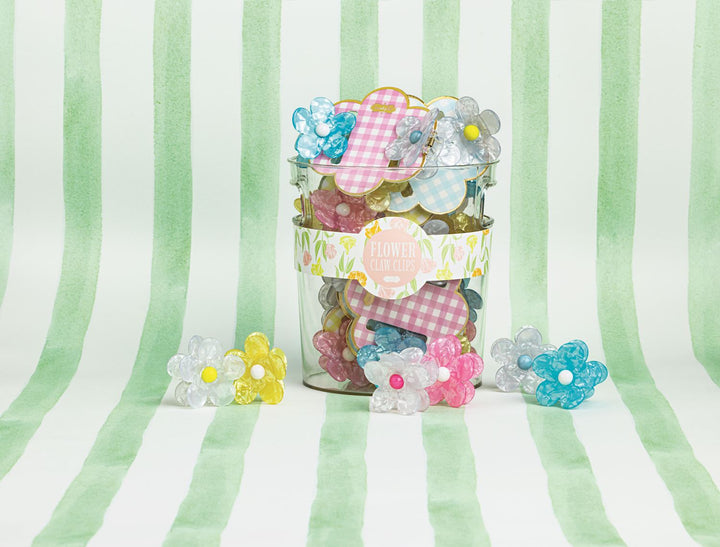 Digital photograph for Mud Pie of marbled flower hair claw clips in a glass jar with a floral label on a green watercolor striped background featuring vibrant yellow centers and pink gingham packaging
