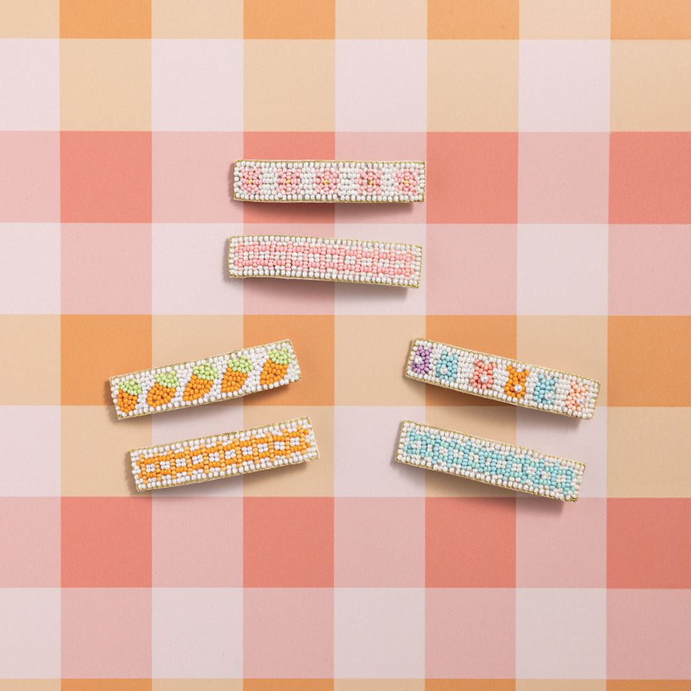 Hand-beaded rectangular hair barrettes are displayed on a pink and orange checkered gingham background featuring colorful citrus fruit patterns, pastel pink stripes, and light blue dots with golden borders