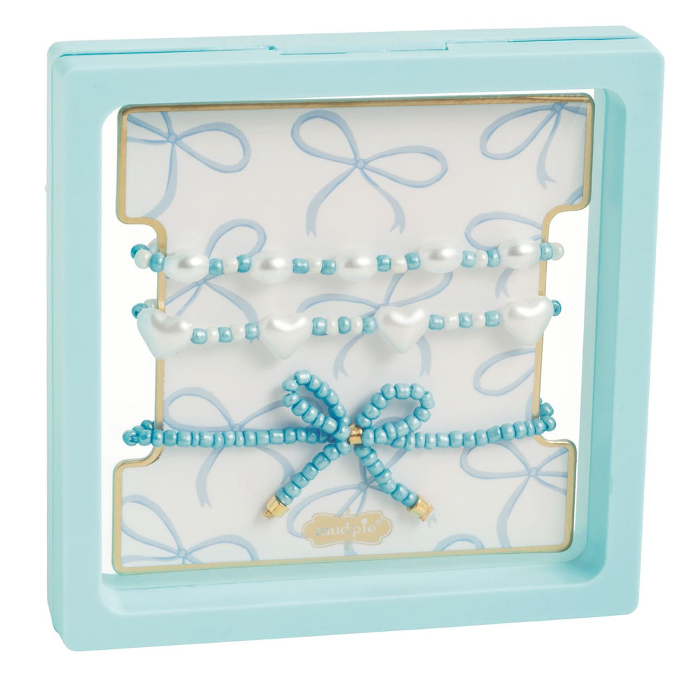 Beaded jewelry set by Mud Pie showcased in a light blue floating frame featuring white heart beads, a central beaded bow, and a blue bow-patterned card insert