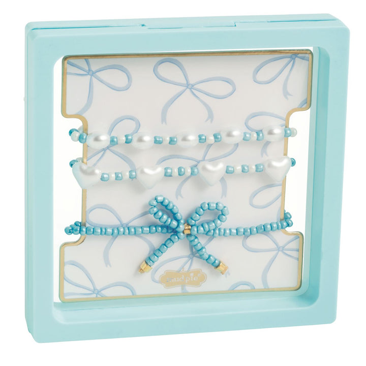 Beaded jewelry set by Mud Pie showcased in a light blue floating frame featuring white heart beads, a central beaded bow, and a blue bow-patterned card insert