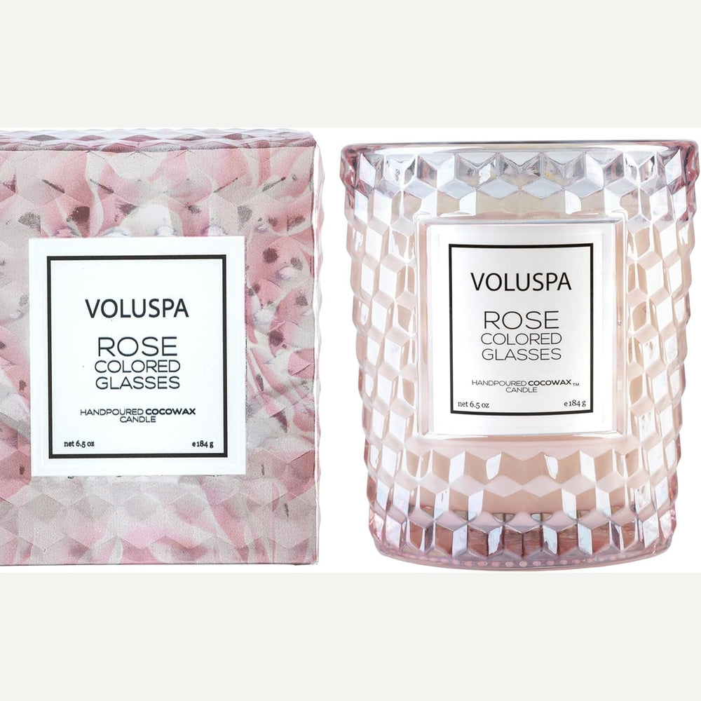 Product photograph by Voluspa of the Rose Colored Glasses candle and its matching gift box featuring a blush-toned honeycomb-textured glass jar, a geometric rose-patterned container, and elegant white labels with black typography