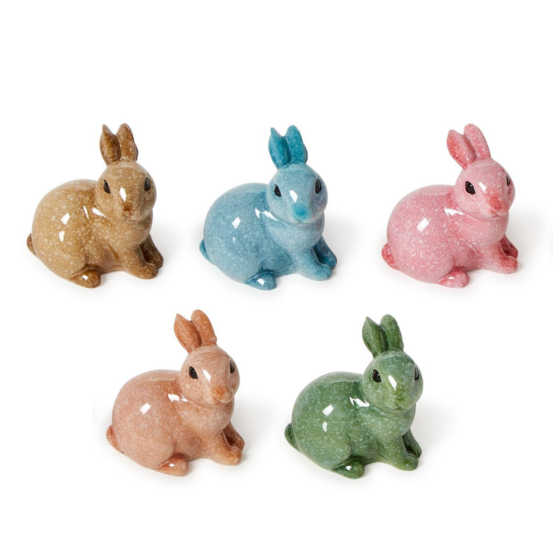 Ceramic figurines of five miniature rabbits with a glossy speckled glaze in shades of tan, blue, pink, peach, and green arranged on a white studio background with small black eyes and polished surfaces