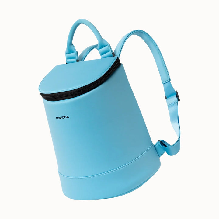 Product photograph by Corkcicle of a sky blue Eola Bucket Cooler Bag in a studio setting featuring the brand logo, a cylindrical silhouette, and a contrasting black zipper with padded straps