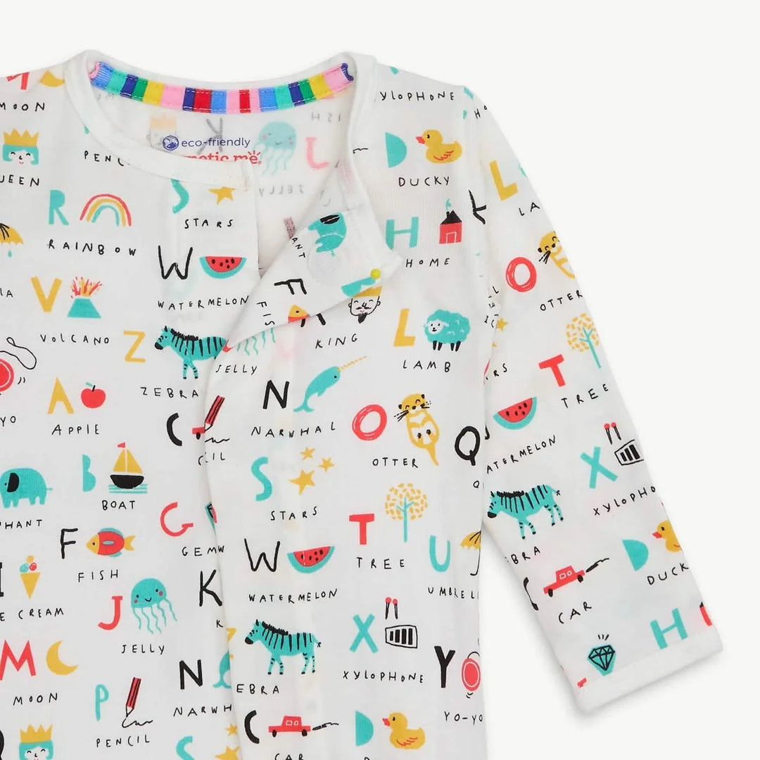 Photograph of a Magnetic Me brand baby onesie featuring an all-over colorful alphabet illustration pattern including a teal zebra, red watermelon slices, and a vibrant rainbow-striped inner neckline