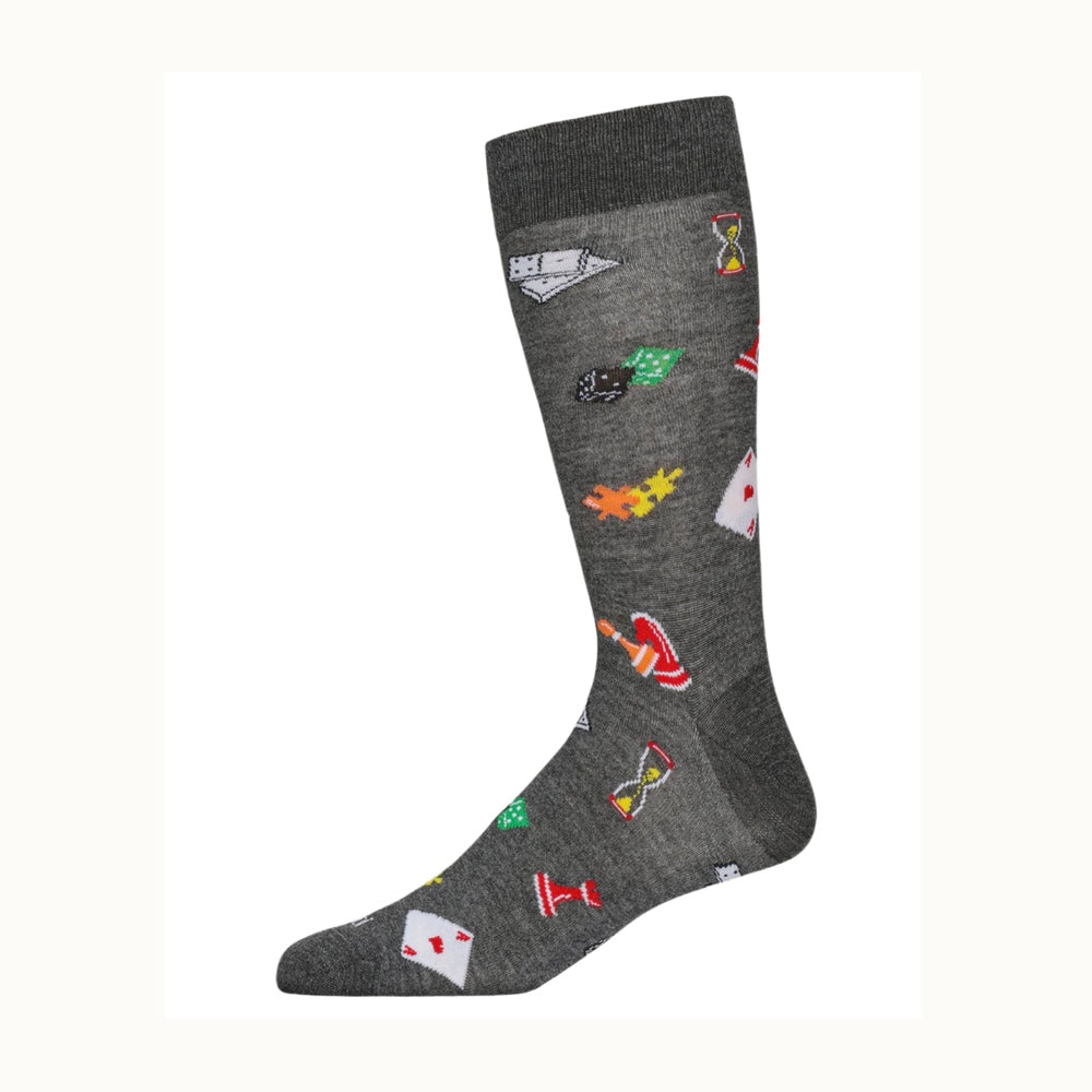 Textile photography of a gray patterned crew sock against a white background featuring board game icons including a red heart playing card, interlocking orange and yellow puzzle pieces, and a yellow hourglass
