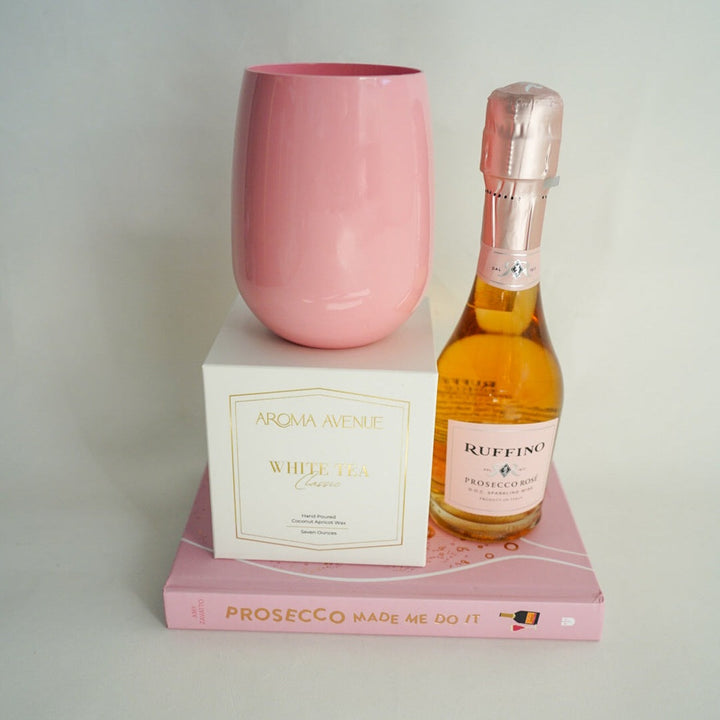 Pink glass, bottle of Prosecco, and box on a white surface