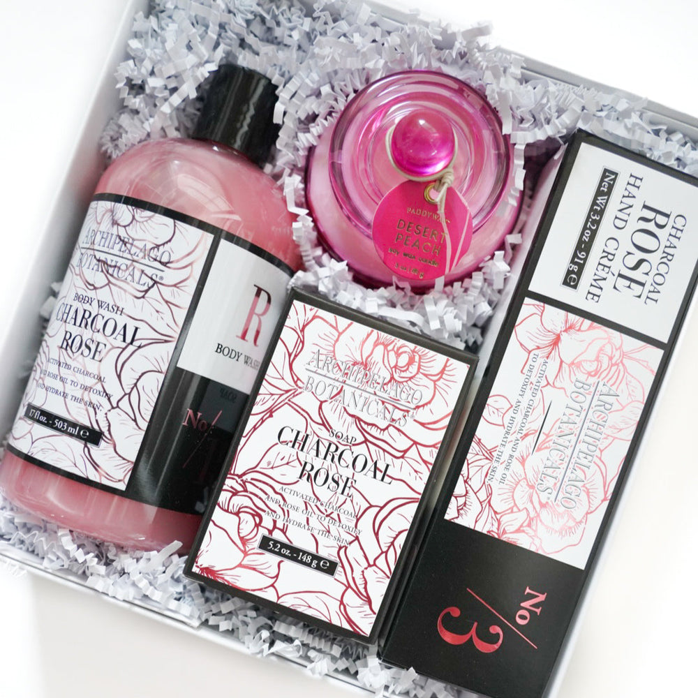 Product photograph of an Archipelago Botanicals Charcoal Rose gift set in a white box featuring pink body wash a vibrant pink Paddywax candle and elegant labels with red floral line art