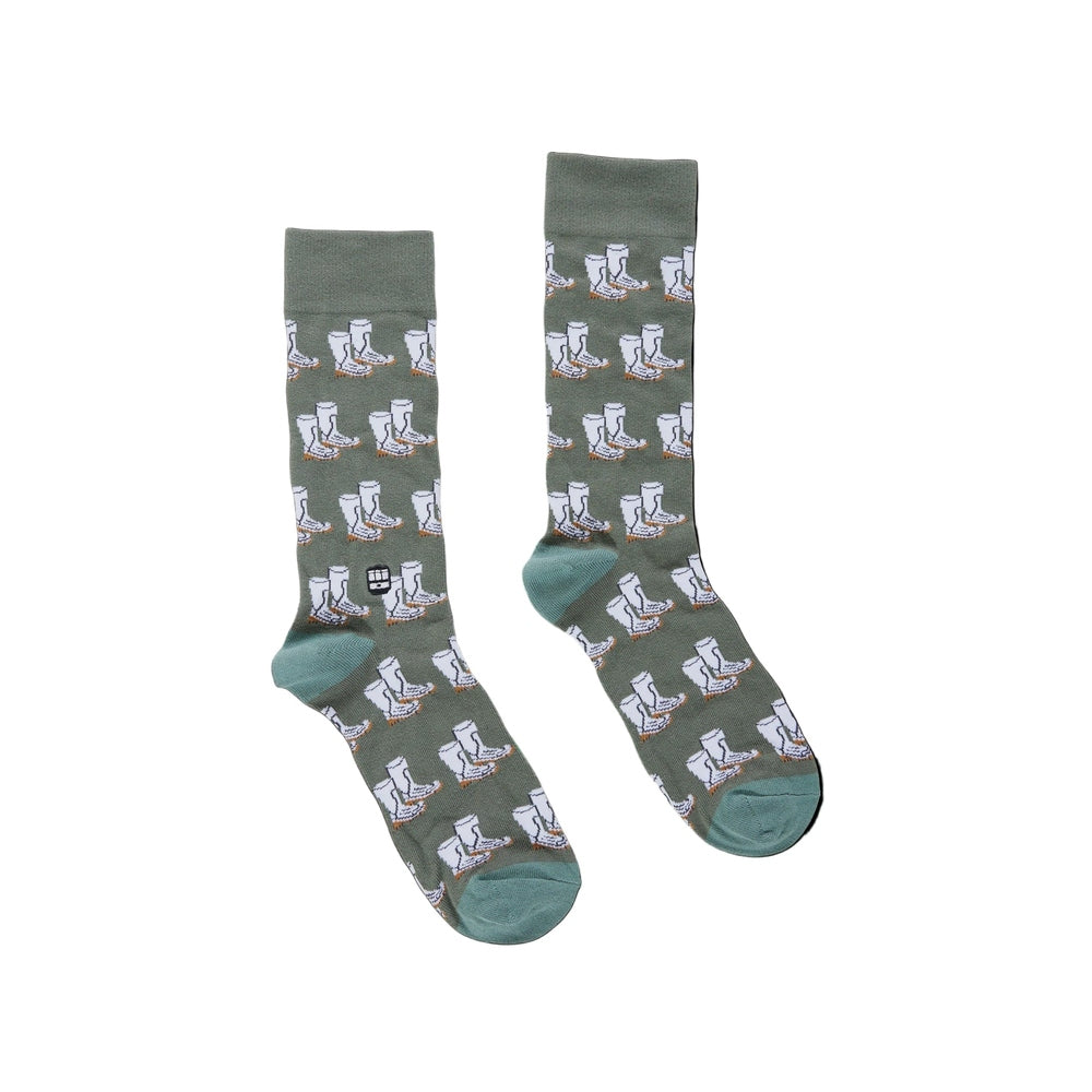 Knit crew socks by The Landmark Project featuring a pair of sage green socks on a white background with a repeating pattern of white work boots with orange soles and light blue heels and toes