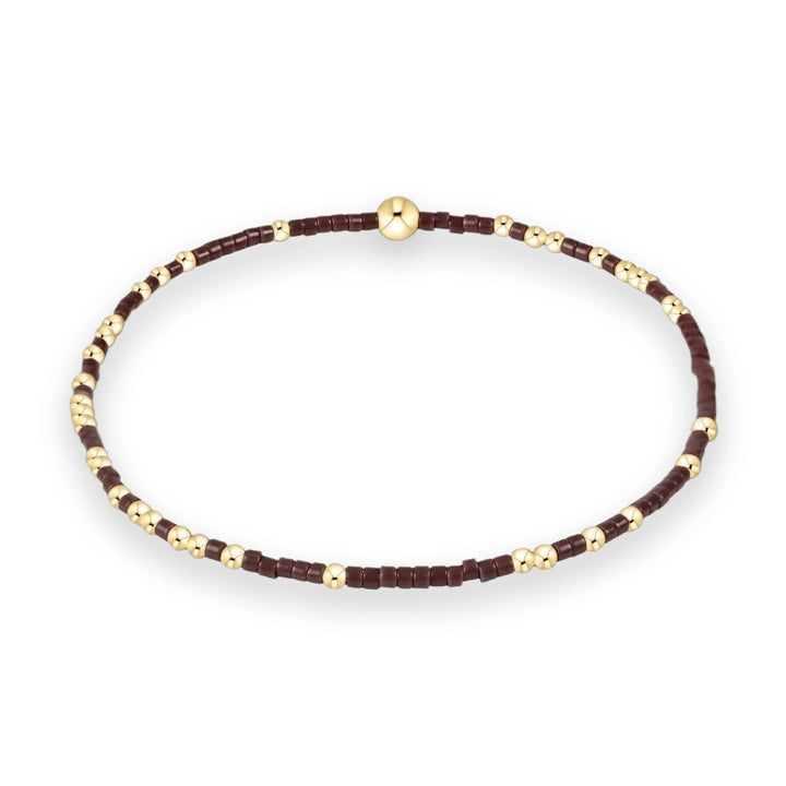 Beaded jewelry handcrafted bracelet on a white background featuring deep maroon cylindrical seed beads interspersed with polished gold spheres and a larger central focal bead