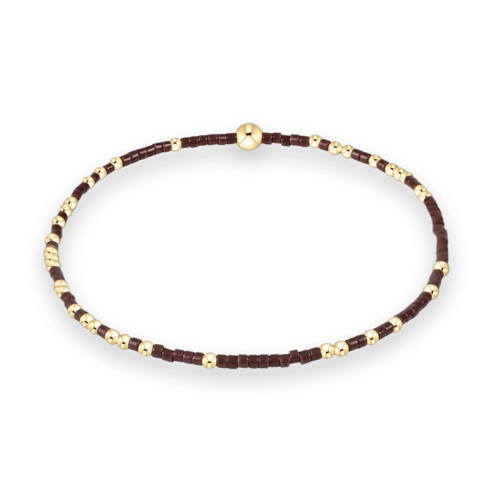 Jewelry design of a beaded stretch bracelet on a plain white background featuring dark brown cylindrical beads accented with polished gold spheres and a single larger central gold bead