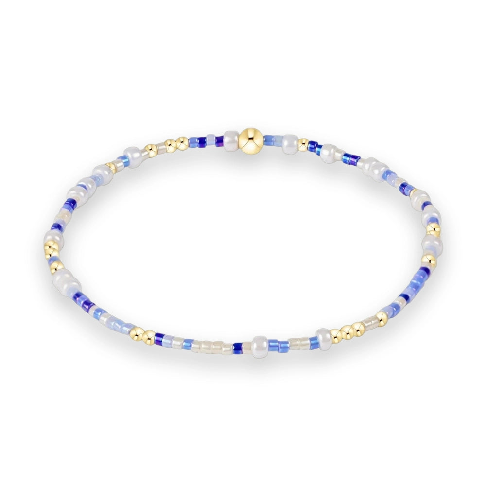 Beaded jewelry handcrafted into a circular bracelet featuring a central polished gold bead accented by cobalt blue, translucent light blue, and iridescent white seed beads on a clean white background
