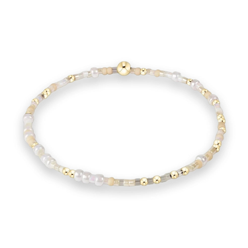 Beaded bracelet featuring a central polished gold bead surrounded by a delicate sequence of pearlescent white, translucent grey, and cream-colored seed beads against a white background
