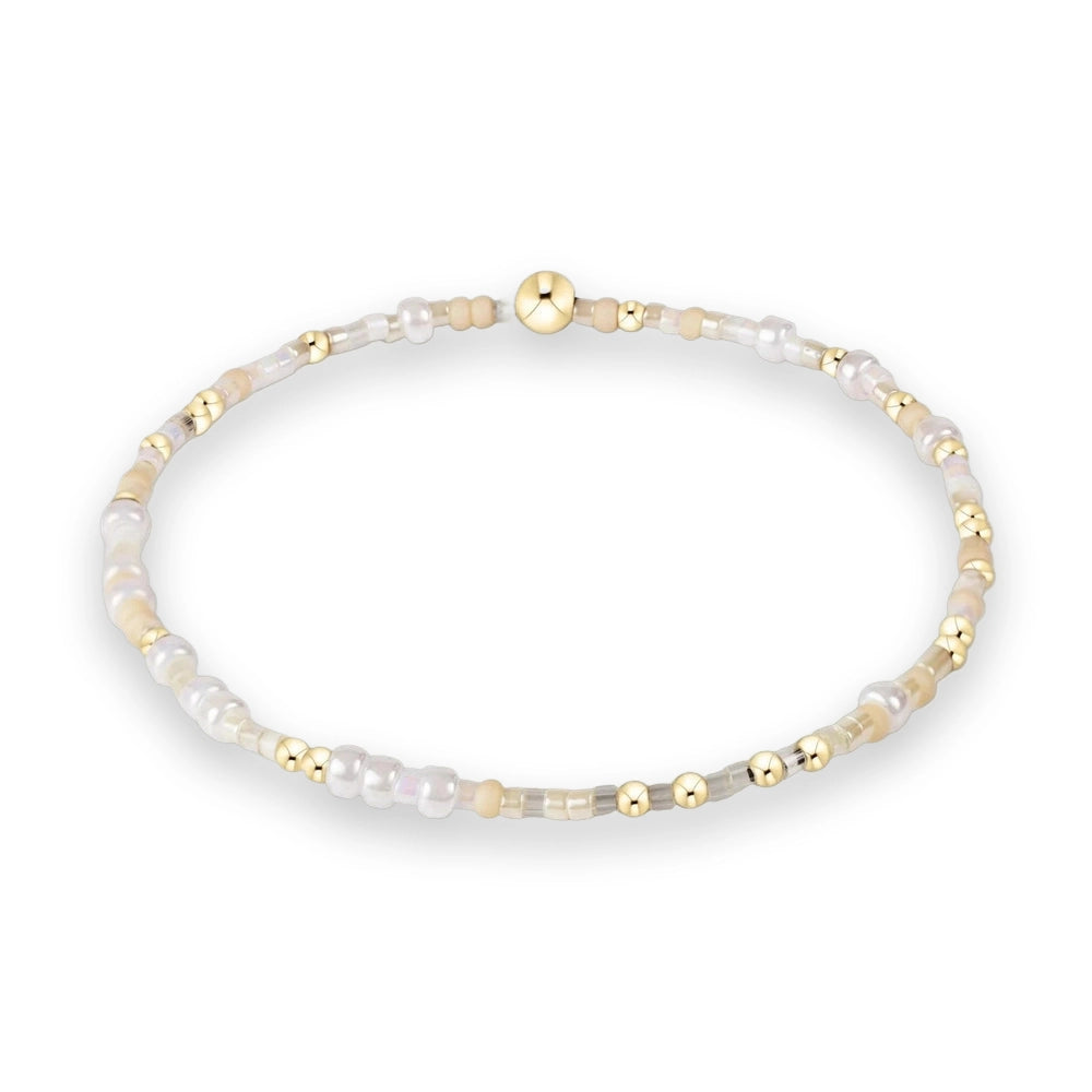 Beaded jewelry featuring a circular bracelet on a white studio background highlighted by a large polished gold bead iridescent white pearls and matte tan accents