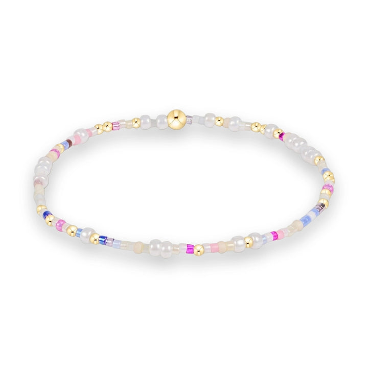 Handcrafted beaded bracelet on a white studio background featuring iridescent white pearls, vibrant pastel pink and lavender accents, and a central polished gold sphere bead