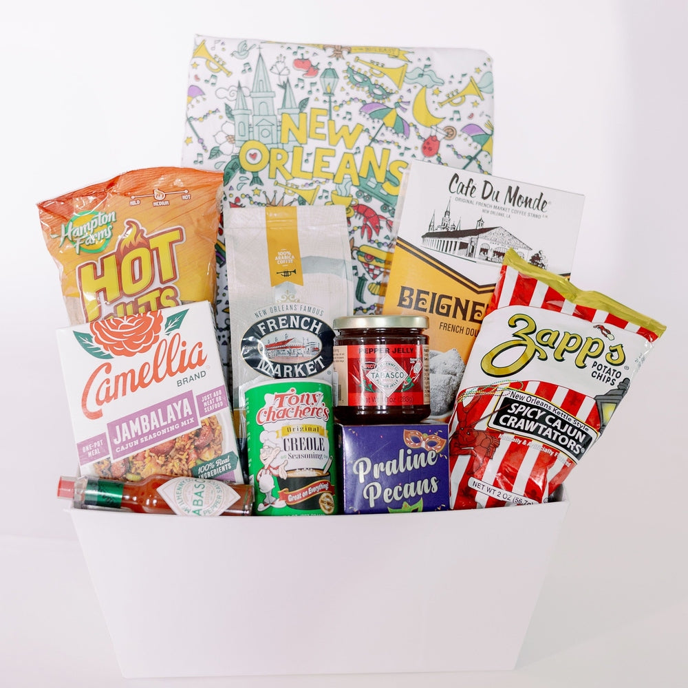 Photograph of a New Orleans gift basket featuring Cafe Du Monde beignet mix and the St. Louis Cathedral alongside red-striped Zapps chips and a purple box of praline pecans decorated with a masquerade mask
